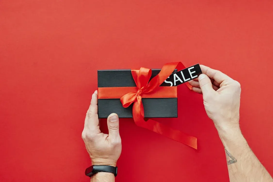 Black gift box with red ribbon and sale tag against a vibrant red background, perfect for promotions