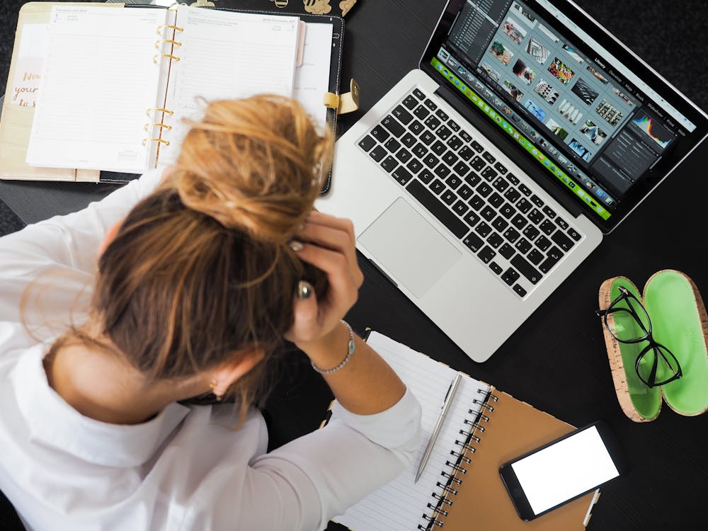 Overhead view of a stressed woman working at a desk with a laptop, phone, and notebooks